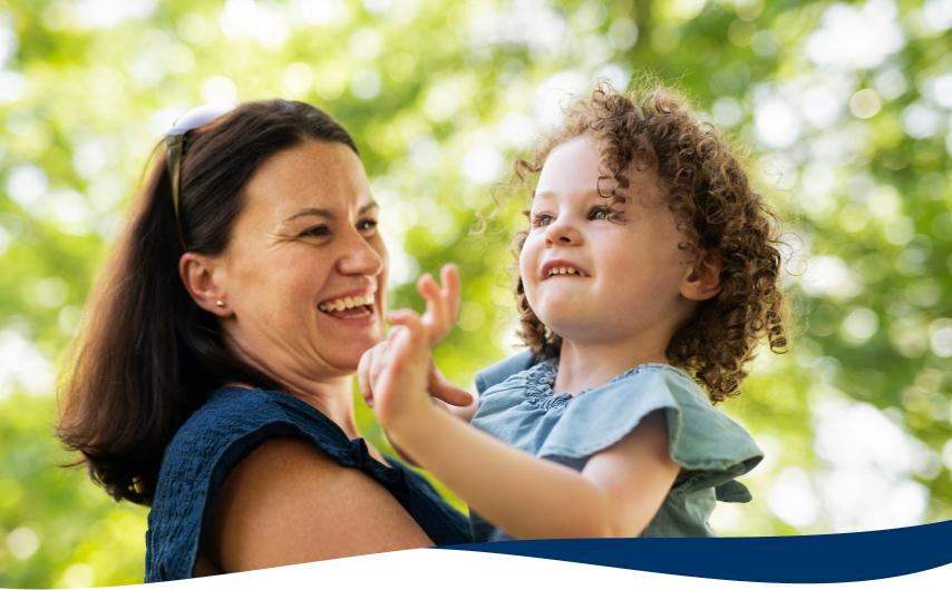 A mother holding her daughter with trees in the background