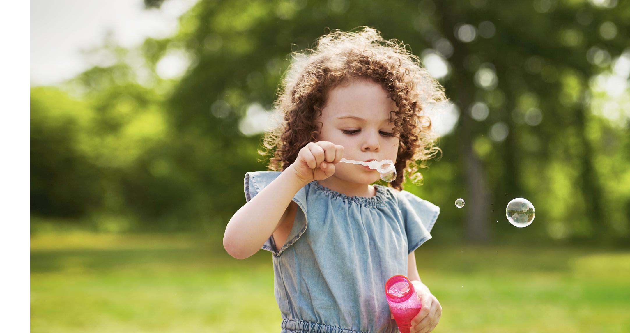A little girl blowing bubbles in a field